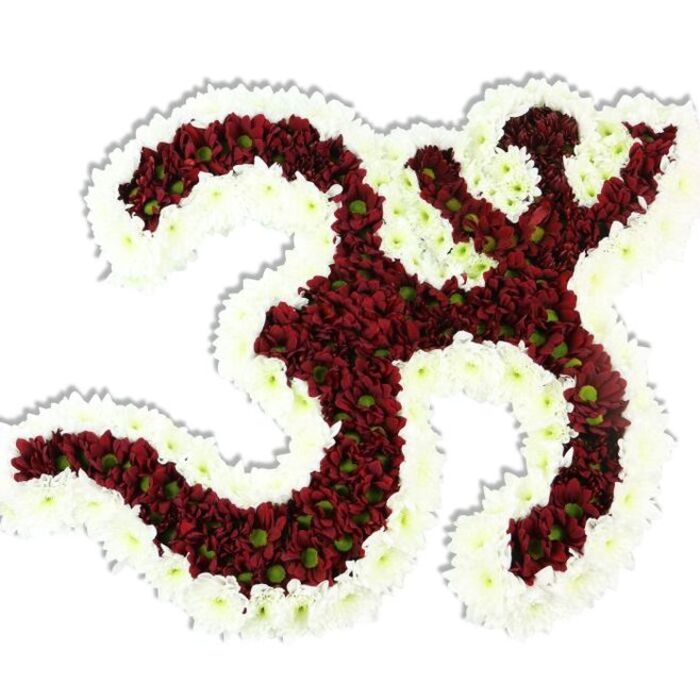 Rendered with meticulous precision, this floral Om (Aum) is a sculptural emblem of silence and presence, photographed against a clean white field that isolates every arc and loop. The body of the symbol is densely filled with deep maroon and dark red chrysanthemum-style blooms; these dozens of small pompon flowers create a voluptuous, velvety plane that defines the '3'-like main curve and the flowing lower stroke with tactile clarity. Each red blossom is punctuated by a small lime-green centre, tiny points of contrast that animate the surface and break the darkness with natural punctuation. Surrounding and tracing the symbol is a broad border of immaculate white spray chrysanthemums, their petite petals forming a smooth, undulating rim that both frames the Om and shapes the negative spaces inside its bends. The overall silhouette is deliberate and refined, the compact petal architecture producing soft highlights and a delicate shadow beneath that confirms the piece's three-dimensional presence. The composition suggests quiet ritual: it could be placed at a devotional display, a yoga or meditation retreat, or as a respectful floral homage at a funeral or commemorative event in local venues from St. George's Hill chapels to community halls in Walton or Addlestone. The tone is one of calm authority-an artworkible tribute made with the discipline of an experienced florist who understands how colour, texture, and form work together to convey spiritual gravity.